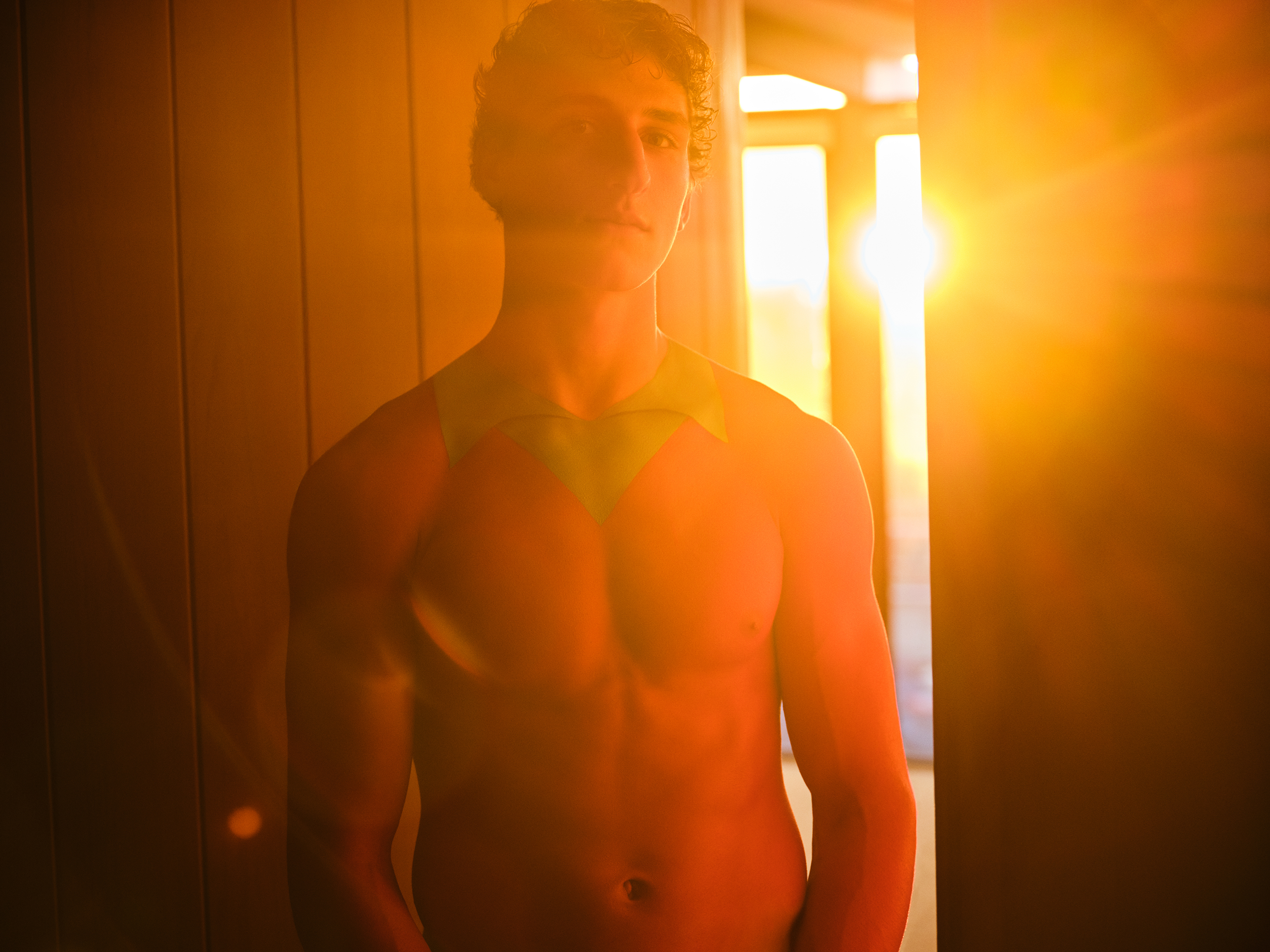 Young man with a red body painted collared shirt looking at the camera against a warm sunset light